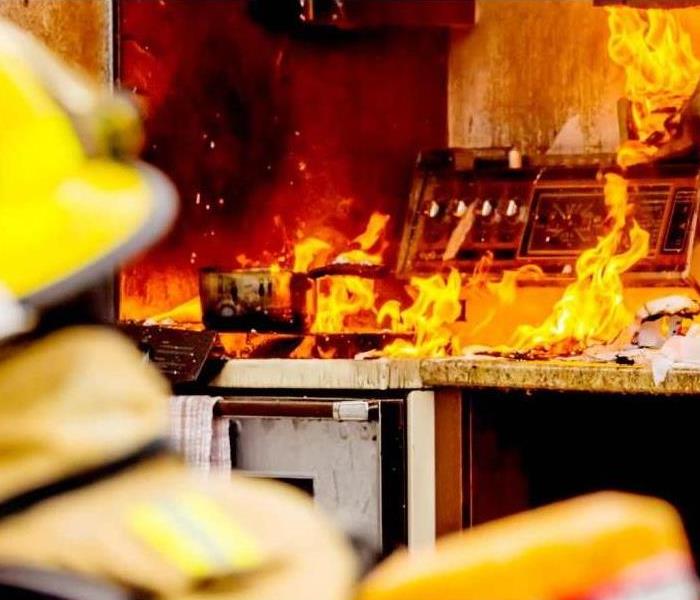 shows a kitchen on fire with a firefighter looking on. 