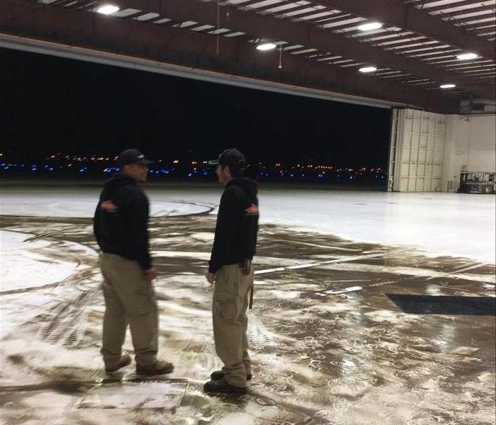 two employees standing in an airplane hangar. Water and dirt smeered on the ground in the background