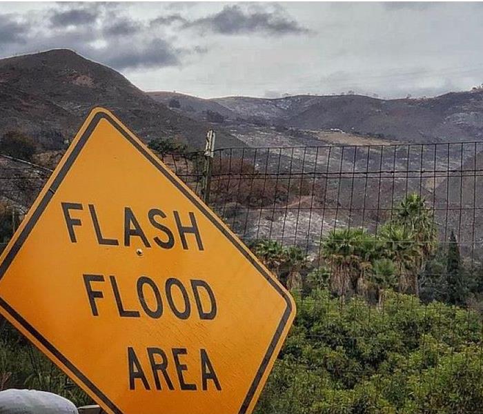 Background shows burned terrain, mountains. Flash Flood Yellow Sign 